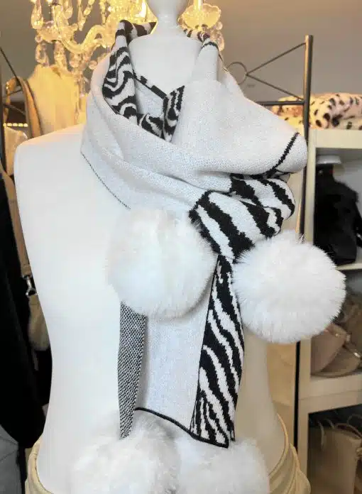 Setz mit dem Wildlook Schal ein Statement: Weich, weiß, zebra-gemustert und mit flauschigen Pom-Poms - dein Hingucker!.