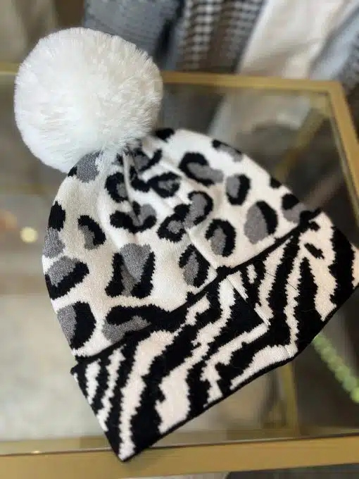 Hol dir den Wildlook: Die stylische Strickmütze im Schwarz-Weiß Animal-Print mit großem weißen Kunstfell-Pompon wartet auf dich!.