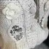 Entdecke deine Belle Amour Strickjacke in Cremeweiß - stylische Stoffknöpfe, Häkelblüte und funkelndes Pailletten-Detail warten auf dich!.