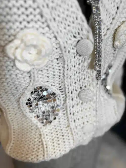 Entdecke deine Belle Amour Strickjacke in Cremeweiß - stylische Stoffknöpfe, Häkelblüte und funkelndes Pailletten-Detail warten auf dich!.