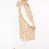 Du trägst eine lange, beige Steppweste über weißem Longsleeve, weiße Hose und Sneaker - modern, lässig, stilsicher.