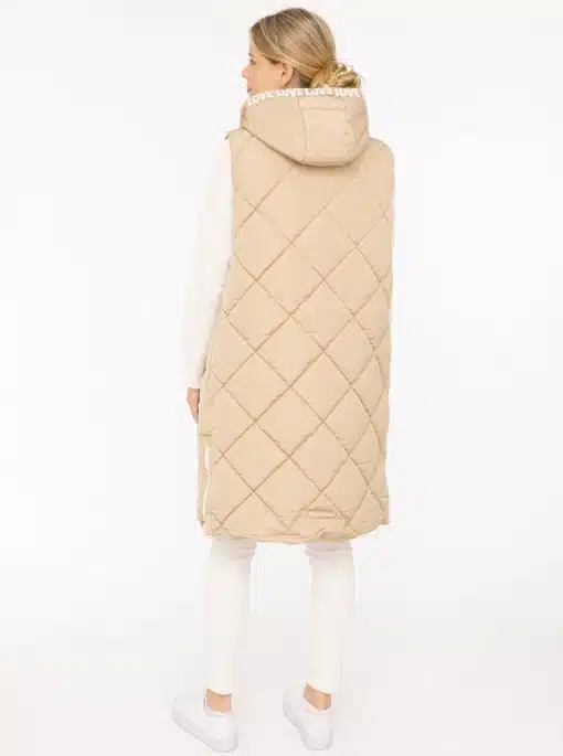 Du trägst eine beige, gesteppte Longweste mit Kapuze, dazu weiße Hose und Sneaker - modern, stilvoll und ganz du selbst.