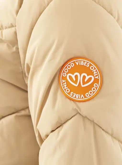 Hol dir den angesagten "Happy Vibes" Steppmantel in Beige - das orange Patch mit "GOOD VIBES ONLY" und Herzen macht dich zum Hingucker!.