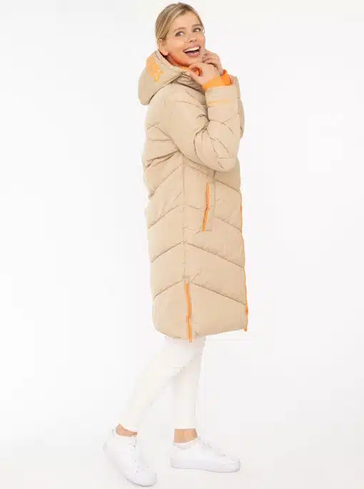 Strahle Glück aus im "Happy Vibes" Steppmantel - lang, beige mit orangen Details. Kombiniere ihn modern mit Weiß und Sneakern.