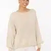 Entdecke deinen modernen Look: Du strahlst in einem lockeren beigen Strickpullover und weißen Hosen vor hellem Hintergrund.