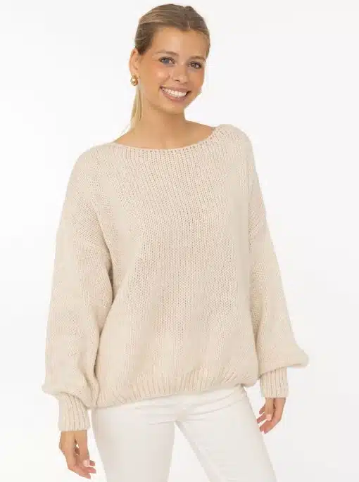 Entdecke deinen modernen Look: Du strahlst in einem lockeren beigen Strickpullover und weißen Hosen vor hellem Hintergrund.