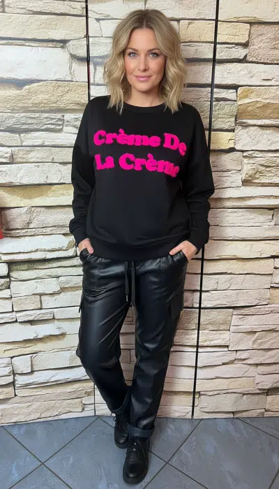 Setze ein Statement mit deinem schwarzen "Crème De La Crème"-Sweatshirt und den angesagten Lederoptik-Jogpants vor Steinwand.