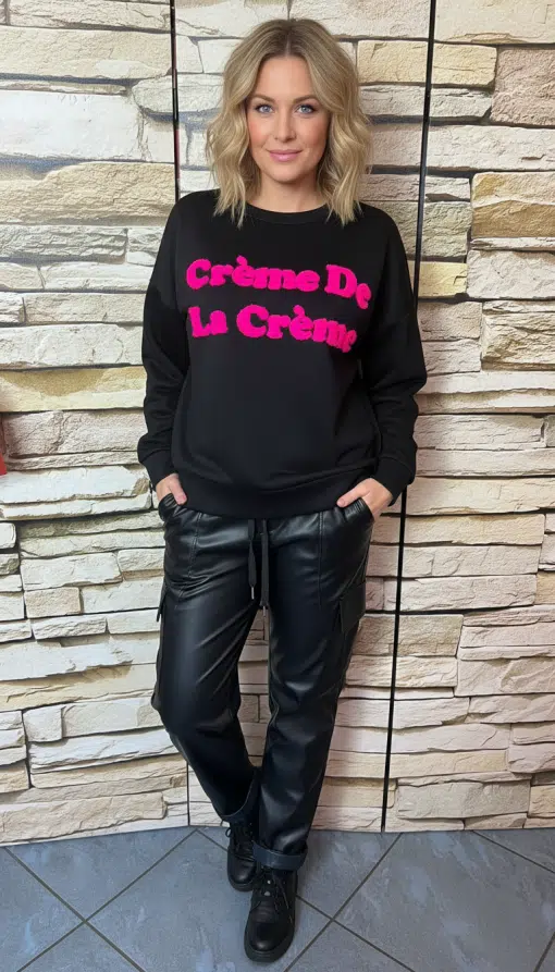 Setze ein Statement mit deinem schwarzen "Crème De La Crème"-Sweatshirt und den angesagten Lederoptik-Jogpants vor Steinwand.