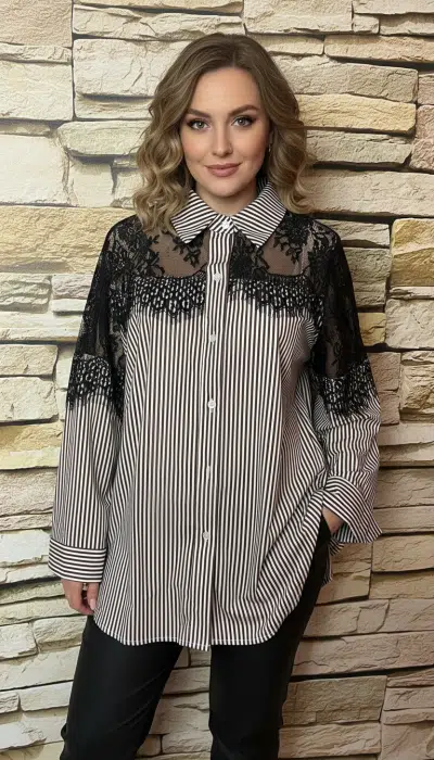 Du strahlst Selbstbewusstsein aus, trägst ein modernes Streifenshirt mit Spitzenakzenten vor urbaner Steinwand und lächelst charmant.