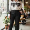 Erlebe den modernen Look: Du trägst die Bella Lace White Bluse, stylishe schwarze Hosen und Boots im angesagten Café am Fenster.