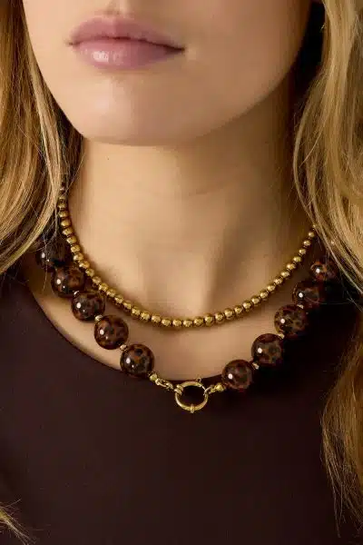 Setze ein Statement mit deinem Look: Trage zwei angesagte Ketten, Gold-Perlen und auffällige Tortoise-Beads auf dunklem Top.