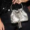 Du hältst eine funkelnde silberne Beuteltasche mit Metallic-Henkel, die perfekt zu deiner schwarzen Hose und dem Paillettentop passt.