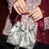 Du trägst funkelnde Herzringe und hältst eine glänzende Silberhandtasche, dazu eine stylische Glitzer-Jacke in Pink und Rot.