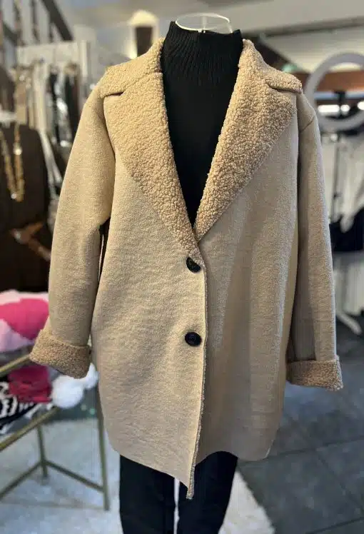 Entdecke deinen neuen Look: Der beige Sherpa-Mantel mit großen Knöpfen und schwarzem Rollkragen macht dich zum Trendsetter.