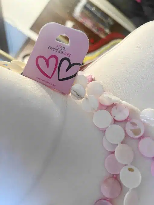 Erlebe die Zwillingsherz Pearl Shine Kette - dein stylisches Must-have in Pink und Weiß, präsentiert mit angesagtem Logo-Tag.