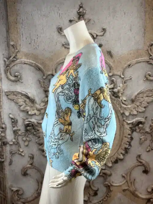 Erlebe den Baroque Angel Cardigan an einem edlen Mannequin mit stilvollen Pastellmustern vor prachtvollem Barock-Setting.