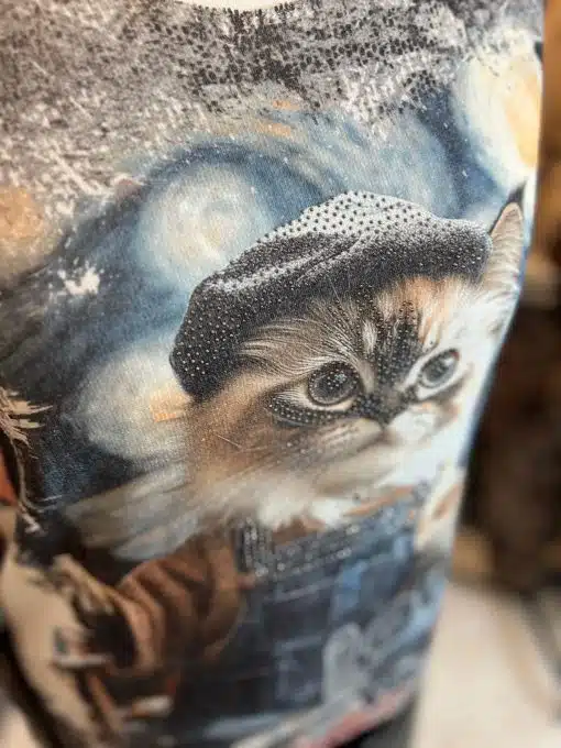 Entdecke dein stylisches Statement: Süßes Kätzchen im coolen Cap und Mantel vor einem trendigen, künstlerischen Hintergrund.