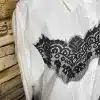 Setze mit der Bella Lace White Bluse und markanten schwarzen Spitzen-Details ein Statement - vor angesagter Backsteinwand.