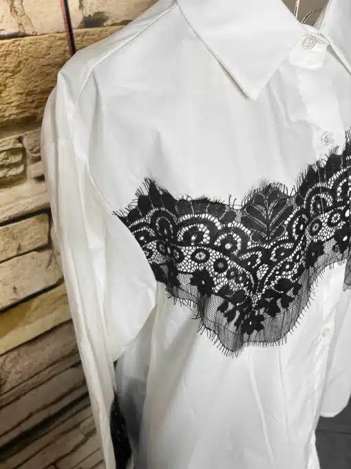 Setze mit der Bella Lace White Bluse und markanten schwarzen Spitzen-Details ein Statement - vor angesagter Backsteinwand.