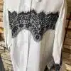 Entdecke die Bella Lace White Bluse - ein moderner Hingucker mit edler schwarzer Spitzenverzierung vor coolem Backstein.