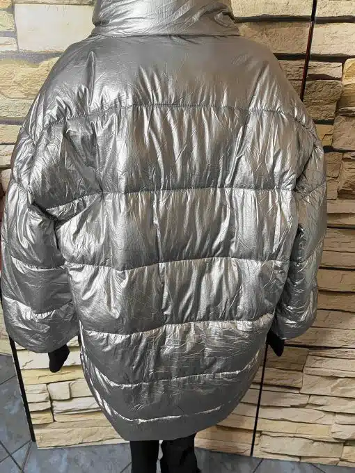 Setzen Sie ein Statement mit der THE BLACK STRIPE Oversize-Jacke im glänzenden Silber-Look vor stylischer Steinwand.