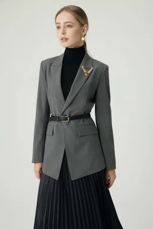Setze stattdessen ein modisches Statement: Du trägst einen grauen Blazer mit Gürtel, schwarzen Rolli, Faltenrock und Hirsch-Brosche.