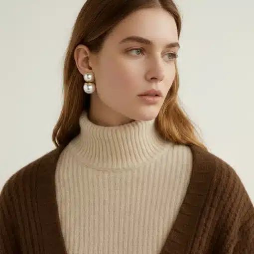 Du trägst einen beigen Rollkragenpullover, eine braune Strickjacke und stilvolle Marit Ohrstecker-Perlen, blickst zur Seite.