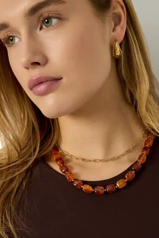 Du trägst ein braunes Top, goldene Ohrringe, eine angesagte Goldkette und eine auffällige Statement-Kette aus Bernstein.