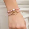 Trage die Zwillingsherz Love Bracelet Twins: Zwei pinke Armbänder, eines mit Herzanhänger, das andere mit weißer Perle.