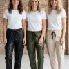 Erlebe deinen Style: Trage weiße Shirts und coole Cargo-Jogpants in Lederoptik wie diese lässigen Frauen vor Backsteinwand.