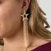 Setzen Sie stilvolle Akzente: Lass deinen Look mit dem Luxus Star Ohrstecker und seinen goldenen Kettentasseln strahlen.