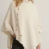 Du stehst im Mittelpunkt: Im cremefarbenen Dinah Poncho mit stylishen Seitenknöpfen und schwarzen Hosen bist du ein Hingucker.