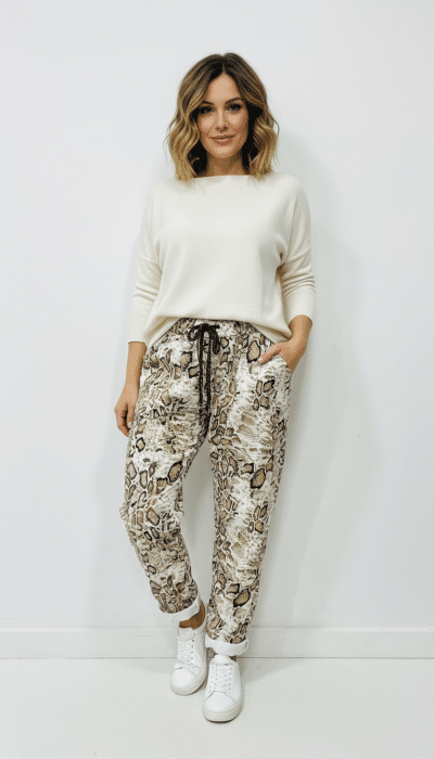 Entdecke deinen Style: Kombiniere weiße Sneaker zum weißen Sweater und zauberhafte Reptile Chic Pants vor heller Wand.