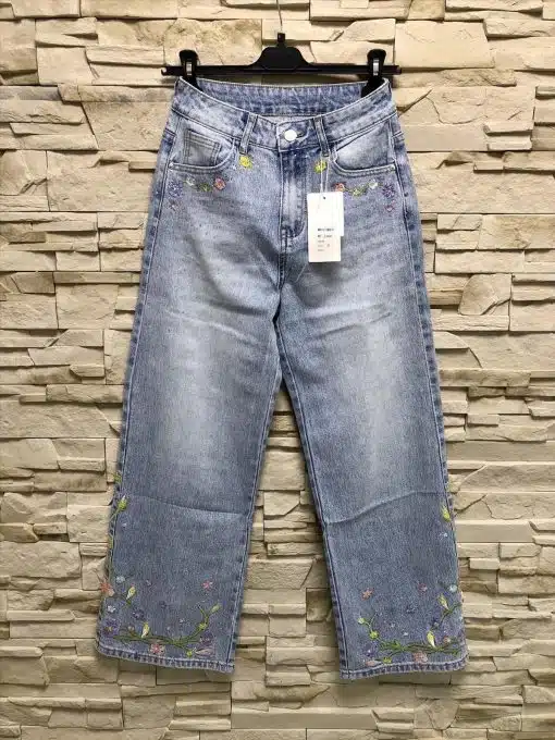 Entdecke deine neue Lieblingsjeans: Hellblaue Jeans mit floralen Stickereien, stilvoll präsentiert vor rustikaler Steinwand.