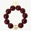Erlebe das GIUNO-Armband: Kraftvolle bordeauxrote Perlen, ein goldener Akzent und gravierte Scheibe für deinen Signature-Look.