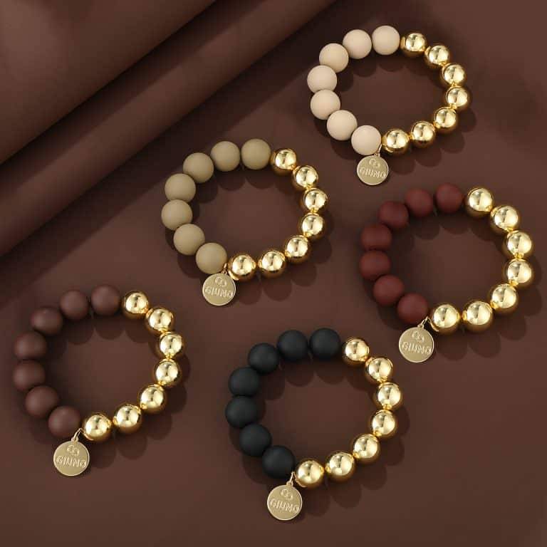 Entdecke deinen Style mit fünf modernen, perlenbesetzten Armbändern und goldenen Akzenten - trendy präsentiert auf braunem Hintergrund.