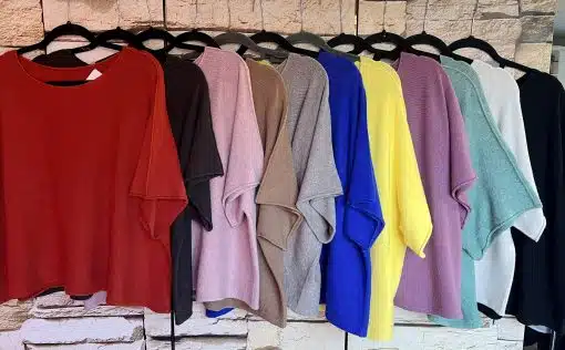 Entdecke deine neuen Lieblingspullover: Soft Touch in lebendigen Farben am schwarzen Bügel vor stilvoller Steinwand!.