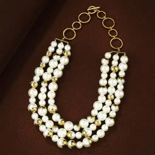 Entdecke dein neues Must-have: Dreireihige Perlen-Goldkette - ein echtes Statement auf braunem, stilvollem Hintergrund.
