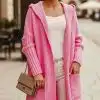 Zeige deinen modernen Stil mit dem langen pinken Simpla Live Cardigan und weißem Outfit - lächelnd draußen mit einer beigen Tasche.