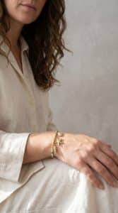 Muschel-Liebe Armband: Goldfarbenes Armband mit Meeresbewohner-Anhängern wie Seestern und Muschel am Handgelenk einer Frau.