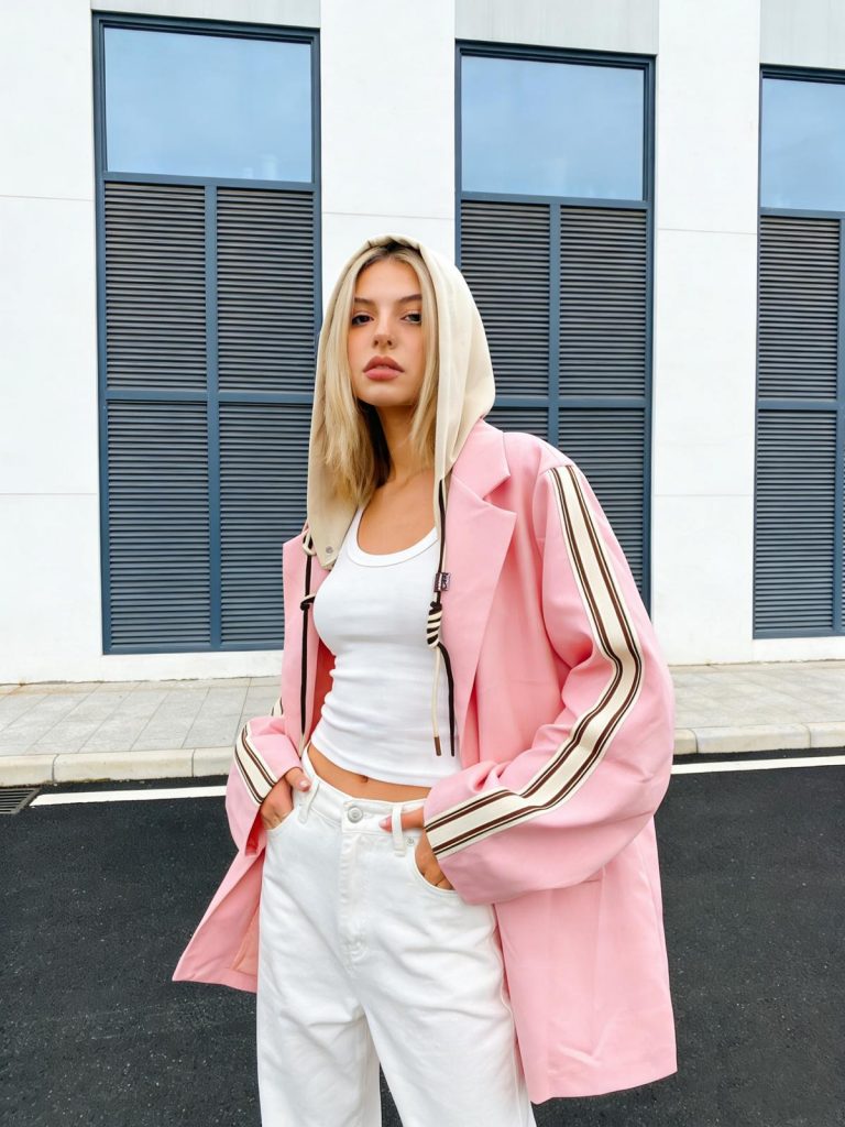 Frau im Freien vor einem modernen Gebäude modelliert City Vibe Hoodie Blazer-rosa gestreifte Ärmel, weißes Tank und Hose für schicken Komfort.