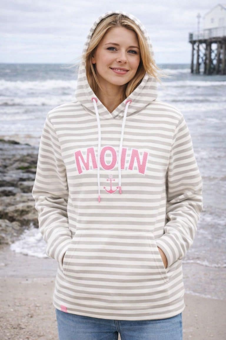 Frau am Strand in Zwillingsherz Damen Hoodie MOIN, hellgrau/weiß gestreift, pinker Druck; gemütlich, stylisch & perfekt für Ausflüge ans Meer.