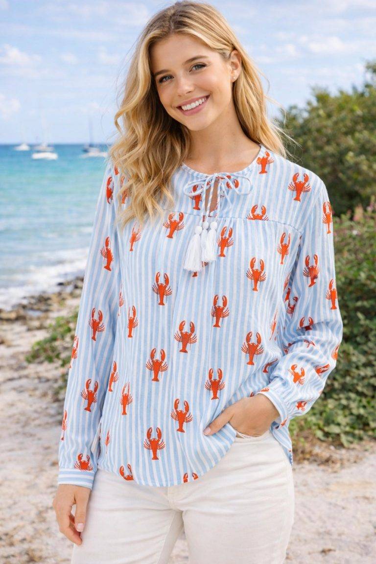 Frau am Strand in Lobsters & Stripes Tunikabluse - hellblau/weiß gestreift, roter Hummerdruck; stilvoller, verspielter Sommermode-Look.