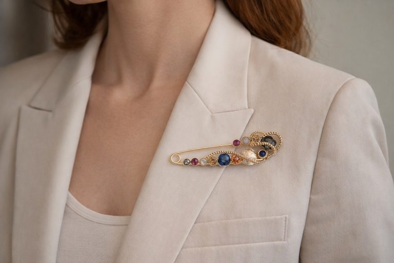 Jewel Dreams Nadel pin on a beige blazer. Gold-tone pin with colorful gemstone accents. Stylish accessory for a touch of elegance.