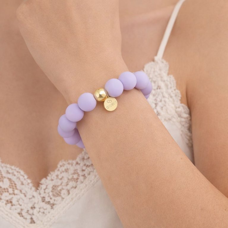 Nahaufnahme des Pastel Glow Armbands mit lavendelfarbenem Band, goldener Perle und rundem Goldanhänger - ein stilvolles Accessoire für den Alltag.