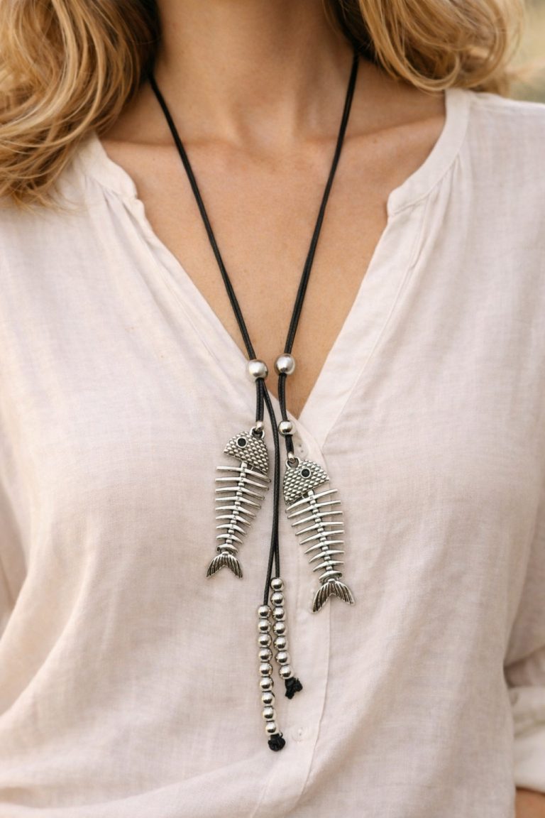 Close-up of a striking silver fishbone necklace with a black cord, complemented by silver beads, against a cream-colored blouse.