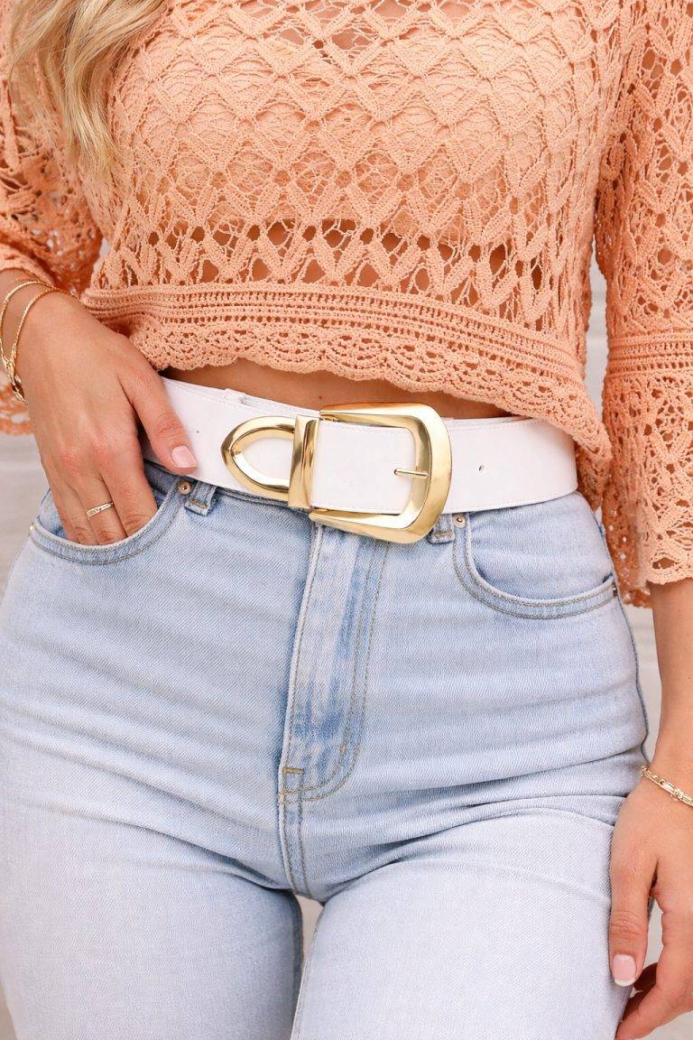 Blanc Gold Gürtel getragen auf hellblauen Jeans. Detailaufnahme des weißen Gürtels mit goldener Schnalle. Model trägt ein orangefarbenes Oberteil.