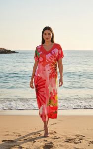 Eine Frau modelliert das Coral Riviera Koffer Kleid, ein farbenfrohes, kurzärmeliges Kleid mit Blumenmuster, das perfekt für den Strand und den Sommer geeignet ist.