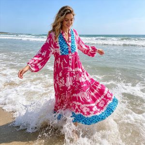 Eine Frau modelliert ein leuchtend rosa und blau gemustertes Maxikleid für den Strand - leicht, fließend, perfekt für Sommerausflüge und mühelosen Stil.