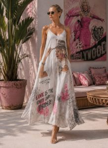 Frau modelliert Promise Glamour Kleid, weißes Kleid mit Rosengrafik und "LOVE IS THE ONLY WAY"-Aufdruck; stilvolle, aufmunternde Mode.